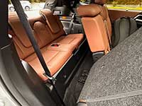Cargo area of a car with orange-brown leather rear seats folded down, gray carpeting, and a visible seat belt.